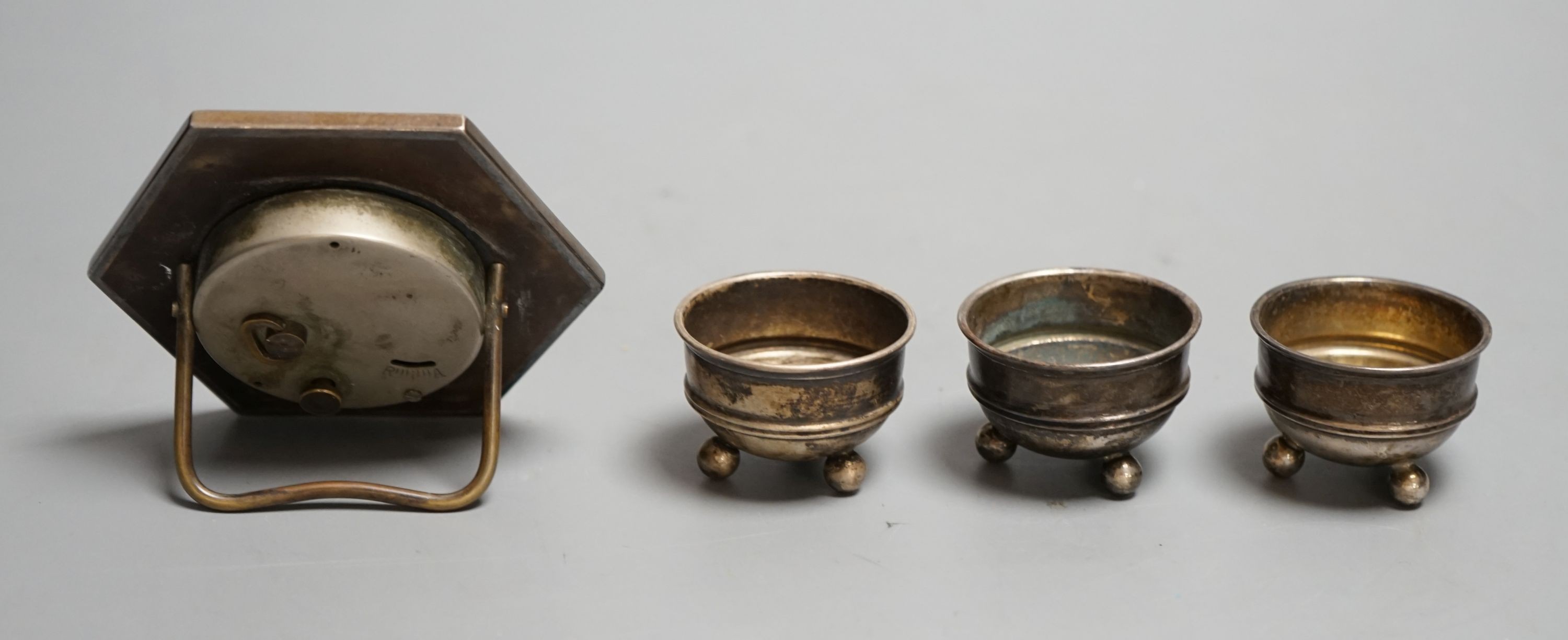 A silver mounted easel strut timepiece and three George V silver salt cellars.